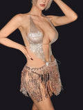 Person wearing a sparkling, semi-sheer top and fringed skirt against a neutral background